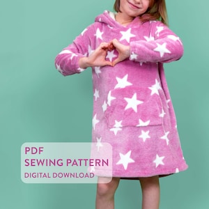 Puede incluir: Una manta con capucha rosa con diseños de estrellas blancas. La manta tiene un gran bolsillo delantero y una textura suave y afelpada. El texto "PDF SEWING PATTERN DIGITAL DOWNLOAD" es visible en la esquina inferior izquierda.