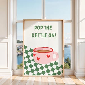 Peut inclure: Une affiche encadrée avec le texte vert POP THE KETTLE ON! au-dessus d'une tasse rose clair ornée de cœurs rouges. La tasse repose sur un motif à damier vert et blanc. L'affiche est présentée dans un cadre en bois clair devant une fenêtre.