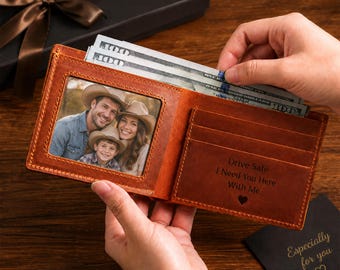 Puede incluir: Una cartera de cuero marrón con una ventana transparente que contiene una foto de una familia con sombreros de vaquero. El interior incluye ranuras para tarjetas y un grabado que dice: Drive Safe I Need You Here With Me.