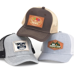 May include: Three trucker hats with mesh backs. One is brown with a tan mesh and a patch that says "LOGO IN HERE". Another is gray with a black mesh and an "EAGLES" patch. The third is light blue with a white mesh and a "SUMMER CAMP" patch.