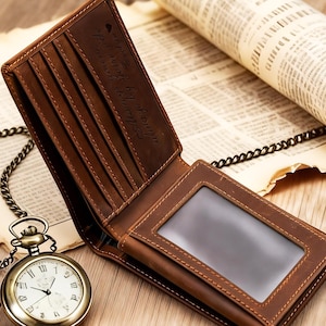 May include: Open brown leather wallet with multiple card slots and a clear ID window. The wallet has a stitched design and the words "Always your side" are embossed on the interior. A vintage pocket watch and chain are in the foreground.