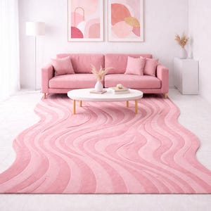 Peut inclure: Un salon moderne avec un canapé rose, une table basse blanche et un tapis rose ondulé. Deux œuvres d'art abstraites encadrées sont accrochées au-dessus du canapé. La pièce est décorée dans des tons de rose et de blanc, créant une atmosphère douce et accueillante.