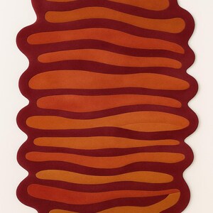 Top view of abstract melted shape rug in burnt orange and deep red tones with organic wavy striped pattern.
