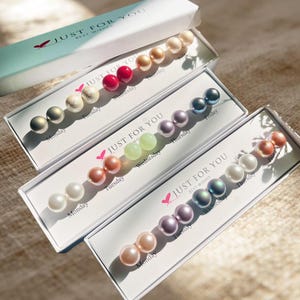 May include: Three rectangular white gift boxes labeled Just For You Best Wishes, each containing five pairs of round stud earrings in various colors. The earrings are arranged in rows, with each pair labeled with a day of the week from Monday to Friday.