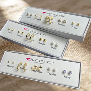 May include: Three white rectangular gift boxes labeled JUST FOR YOU BEST WISHES, each containing five pairs of gold-tone earrings organized by days of the week. The sets include various stud, hoop, pearl, butterfly, and crystal-embellished designs.