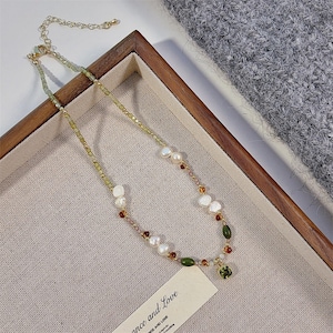 Puede incluir: Un collar que presenta una mezcla de pequeñas cuentas facetadas de color verde claro, perlas de agua dulce blancas irregulares, cuentas ovaladas de color verde oscuro y pequeñas piedras de color ámbar. Incluye una cadena extensora dorada y un colgante cuadrado verde.