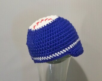 Può includere: Un cappello blu lavorato all'uncinetto con un design bianco e rosso sulla parte superiore e un bordo bianco. Il cappello è fatto di un filato spesso e ha una tesa. Il cappello è su un bicchiere trasparente.