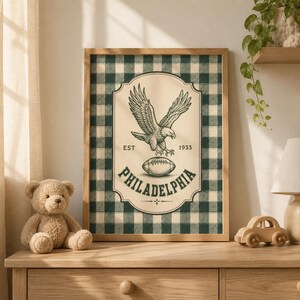 Pu&ograve; includere: Una stampa artistica incorniciata con uno sfondo a quadri verde scuro e crema. Il grafico centrale mostra un'aquila sopra un pallone da football con il testo EST 1933 e PHILADELPHIA stampato in un carattere serif verde scuro entro un bordo decorativo.