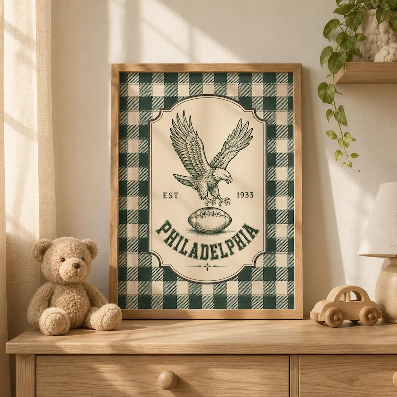 Pu&ograve; includere: Una stampa artistica incorniciata con uno sfondo a quadri verde scuro e crema. Il grafico centrale mostra un'aquila sopra un pallone da football con il testo EST 1933 e PHILADELPHIA stampato in un carattere serif verde scuro entro un bordo decorativo.