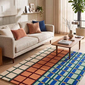 Puede incluir: Una alfombra rectangular con un patrón geométrico de cuadrícula. El diseño se divide en tres secciones verticales con cuadrados de color crema, naranja quemado y una combinación de azul y verde, acentuados por líneas oscuras.