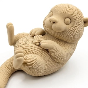 Könnte beinhalten: Hellbraune, 3D-gedruckte Otter-Figur, die auf dem Rücken liegt und eine Muschel hält. Der Otter hat eine strukturierte Oberfläche, mit ausgestreckten Pfoten und Schwanz. Die Figur ist ein dekorativer Artikel.