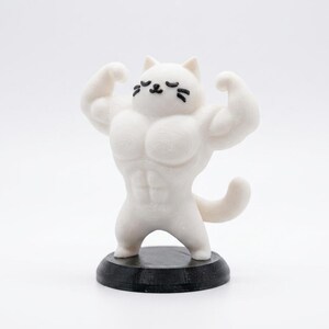 Può includere: Statuetta bianca di un gatto muscoloso che flette le braccia. Il gatto ha segni neri per gli occhi e i baffi. Si trova su una piccola base rotonda nera. Il fisico del gatto è esagerato, con muscoli definiti.