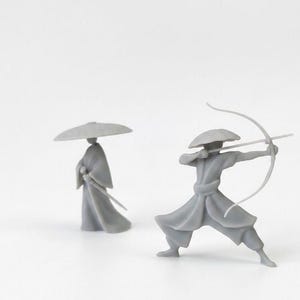 Puede incluir: Dos figuras grises en miniatura de guerreros japoneses. Una figura está de pie con una espada, y la otra está en posición de disparo con arco y flecha. Ambas figuras visten sombreros y ropa tradicionales.