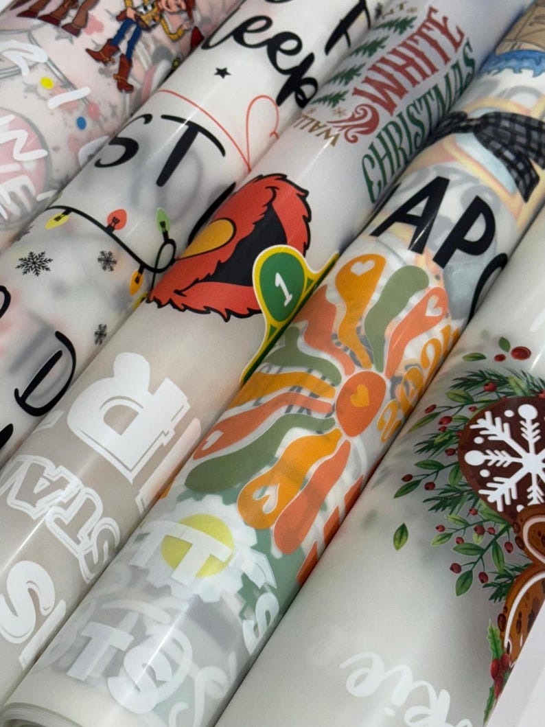 May include: A collection of rolled-up patterned papers, featuring various designs. Some rolls display text like "STARS" and "WHITE CHRISTMAS." Other designs include a retro flower, a cartoon character, and holiday-themed graphics. The papers are in shades of white, beige, and various colors.