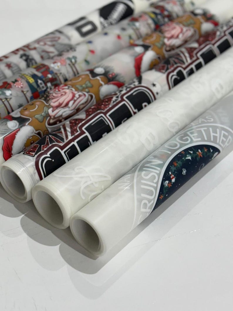 May include: Several rolls of decorative wrapping paper with holiday-themed designs. The patterns include Santa Claus, gingerbread men, and festive text. The rolls are white and have various colors.