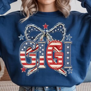 May include: Navy blue sweatshirt with a patriotic design. The design features the word "GIGI" in red and white stripes, surrounded by a bow and stars, all in a red, white, and blue color scheme. The sweatshirt is a comfortable, casual style.
