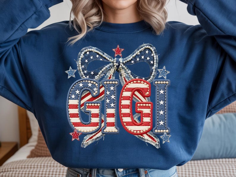 May include: Navy blue sweatshirt with a patriotic design. The design features the word "GIGI" in red and white stripes, surrounded by a bow and stars, all in a red, white, and blue color scheme. The sweatshirt is a comfortable, casual style.