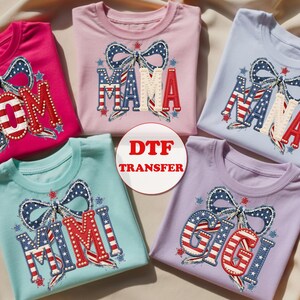 May include: Five colorful t-shirts with patriotic designs. Each shirt features a bow and a different name: MOM, MAMA, NANA, MIMI, and GIGI, in red, white, and blue. The shirts are in shades of pink, blue, and purple, perfect for family.