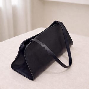 Minimalist women leather bag in black with structured baguette bag silhouette, sleek shoulder bag featuring smooth genuine leather and curved design, elegant top handle handbag with crossbody strap option, aesthetic bag inspired by 90s baguette bag and pinterest trends, everyday bag for casual and work use, zipper closure leather purse with compact functionality, classic handbag with quiet luxury style, minimalist work bag and trendy everyday bag, perfect gift for women