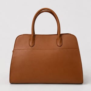 May include: A structured tan handbag with a smooth finish, featuring two rounded top handles attached to the main body with reinforced stitching. The bag has a wide, flat base and a horizontal seam detail across the front panel of the exterior.