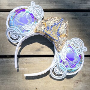 May include: White headband with a gold and silver glitter castle and a purple and silver glitter carriage on each side. The castle has a blue "50" on it.