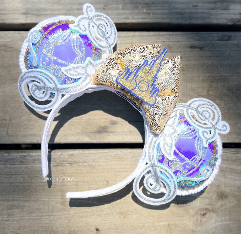 May include: White headband with a gold and silver glitter castle and a purple and silver glitter carriage on each side. The castle has a blue "50" on it.
