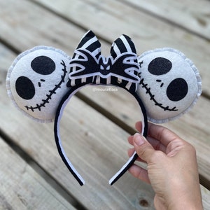 May include: Black and white striped bow with a bat design, attached to a white headband with two white felt ears featuring a black and white Jack Skellington face.  @mousetiara