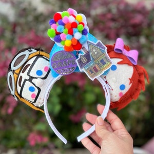 May include: Up themed Minnie Mouse ears with a felt character of Carl Fredricksen and Russell, a house, a bunch of balloons, and a Grape Soda pin.