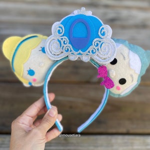 May include: Cinderella and Prince Charming character ears with a blue and silver carriage headband. The headband is decorated with glitter and the characters have pink cheeks.