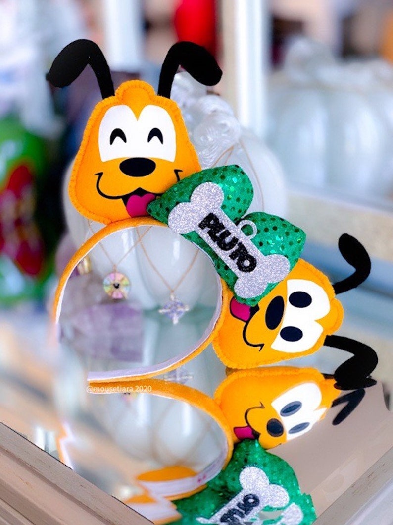 Peut inclure: Un serre-t&ecirc;te en feutre jaune et noir avec un personnage en peluche de Pluto portant un n&oelig;ud vert et argent&eacute; paillet&eacute; avec un os sur lequel est &eacute;crit "Pluto".