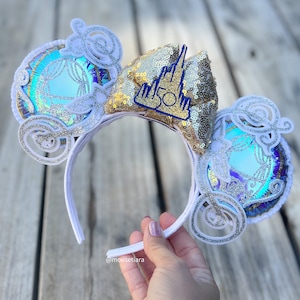 May include: White headband with a gold and blue bow featuring a Cinderella carriage and the text "50th" on the bow.
