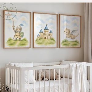 May include: Three framed watercolour prints depicting a knight, a castle, and a dragon, set against a blue sky with clouds. The prints are displayed above a white cot with a teddy bear and a blanket. A stuffed bunny sits in a basket.