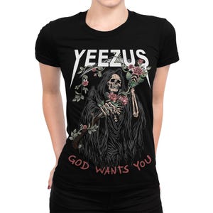 May include: Black t-shirt with the word "YEEZUS" in white, above a graphic of a Grim Reaper holding roses. The phrase "GOD WANTS YOU" is printed in pink below the graphic. The design is centered on the shirt.