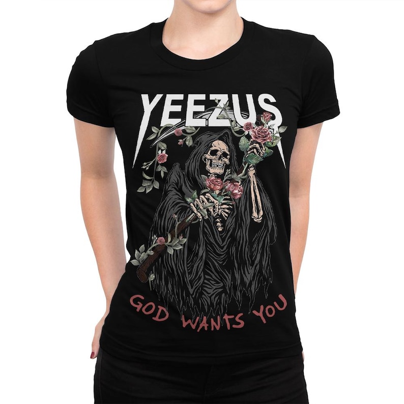 May include: Black t-shirt with the word "YEEZUS" in white, above a graphic of a Grim Reaper holding roses. The phrase "GOD WANTS YOU" is printed in pink below the graphic. The design is centered on the shirt.