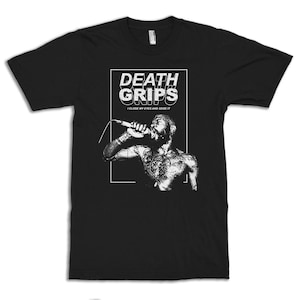 May include: Black t-shirt featuring a white graphic of a person singing into a microphone. The graphic includes the band name "DEATH GRIPS" and the text "I CLOSE MY EYES AND SEIZE IT". The person in the graphic has tattoos.