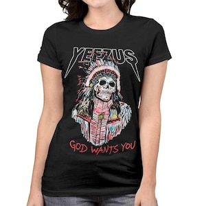Peut inclure: T-shirt noir avec un motif de cr&acirc;ne portant une coiffe am&eacute;rindienne. Le mot "YEEZUS" est au-dessus du cr&acirc;ne, et "GOD WANTS YOU" est en dessous. Le design utilise des couleurs rouge, bleu, rose et blanc.