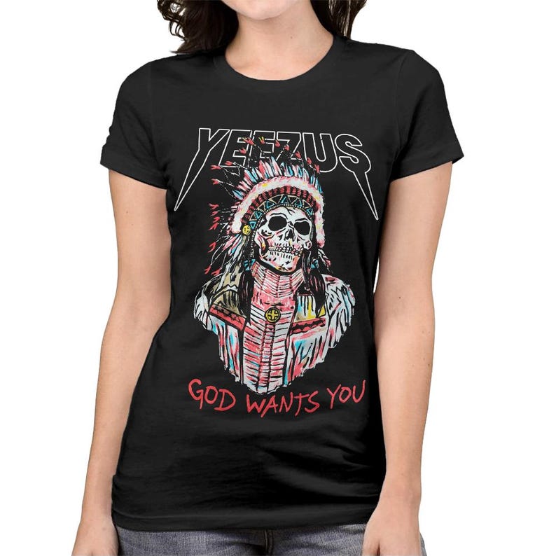 Peut inclure: T-shirt noir avec un motif de cr&acirc;ne portant une coiffe am&eacute;rindienne. Le mot "YEEZUS" est au-dessus du cr&acirc;ne, et "GOD WANTS YOU" est en dessous. Le design utilise des couleurs rouge, bleu, rose et blanc.