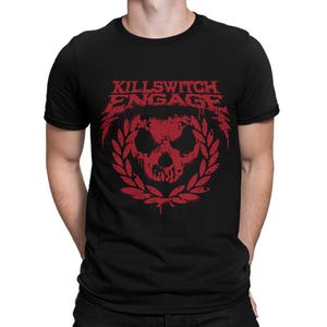 Può includere: T-shirt nero con grafica rossa. Il design presenta il nome della band "Killswitch Engage" sopra un teschio all'interno di una corona d'alloro. La grafica ha un aspetto invecchiato e strutturato.