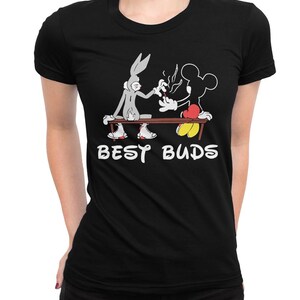 May include: Black t-shirt with a graphic of Bugs Bunny and Mickey Mouse sharing a cigarette, with the words "BEST BUDS" in white. The cartoon characters are seated on a bench. The shirt has a crew neck.