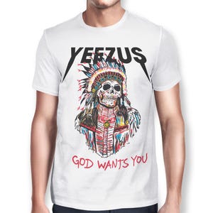 Peut inclure: T-shirt blanc avec un motif de cr&acirc;ne portant une coiffe am&eacute;rindienne. Le mot "YEEZUS" est imprim&eacute; en noir au-dessus du cr&acirc;ne, avec la phrase "GOD WANTS YOU" en rouge en dessous.