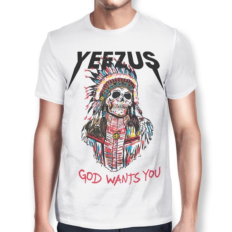 Peut inclure: T-shirt blanc avec un motif de cr&acirc;ne portant une coiffe am&eacute;rindienne. Le mot "YEEZUS" est imprim&eacute; en noir au-dessus du cr&acirc;ne, avec la phrase "GOD WANTS YOU" en rouge en dessous.
