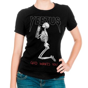 May include: Black t-shirt with the word "YEEZUS" in white, above a skeleton kneeling in prayer. The text "GOD WANTS YOU" is printed in red below the skeleton. The shirt is short-sleeved.