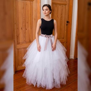 May include: A black sleeveless top paired with a layered white tulle skirt. A satin ribbon in a neutral color cinches the waist. The outfit is suitable for special occasions, such as a wedding or a dance performance.