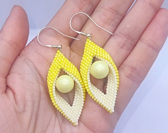 May include: A pair of yellow and white beaded earrings with a pearl-like bead in the center of each earring.