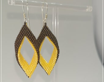 May include: A pair of dangle earrings with a yellow and brown geometric design. The earrings are displayed on a clear stand.