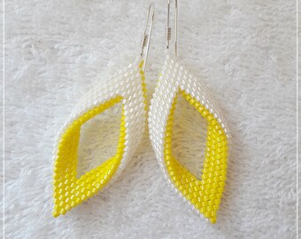 May include: A pair of yellow and white beaded earrings with silver hooks. The earrings are shaped like a twisted leaf.