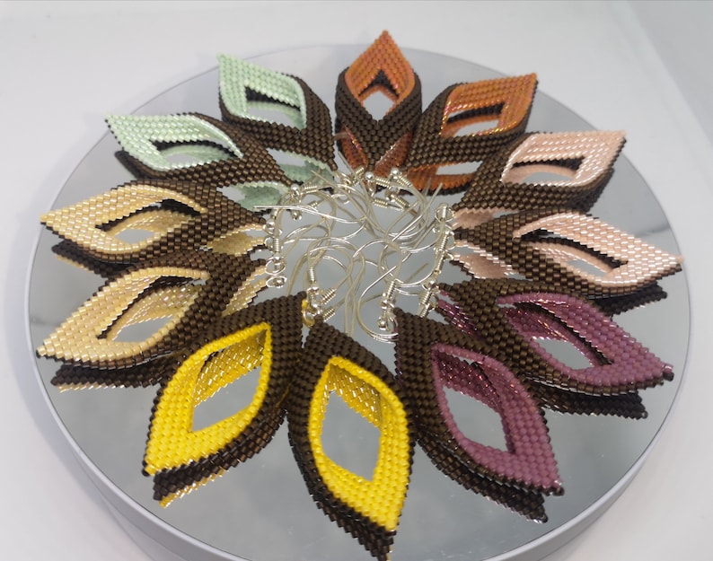 May include: A set of 10 pairs of beaded earrings in various colors, including brown, yellow, pink, and green. Each earring is shaped like a leaf with a cut-out design in the center.