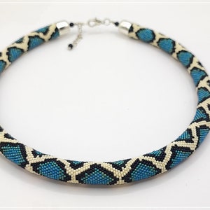 May include: A blue and white beaded necklace with a snake skin pattern. The necklace is made of small beads and has a silver clasp.