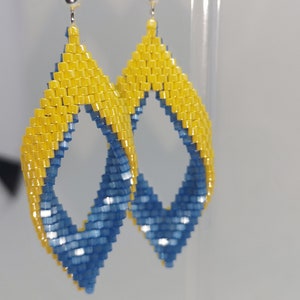 May include: A pair of dangle earrings with a blue and yellow geometric design. The earrings are made of small beads and have a silver hook.