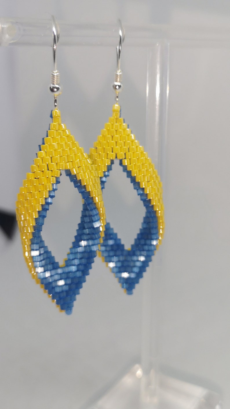 May include: A pair of dangle earrings with a blue and yellow geometric design. The earrings are made of small beads and have a silver hook.